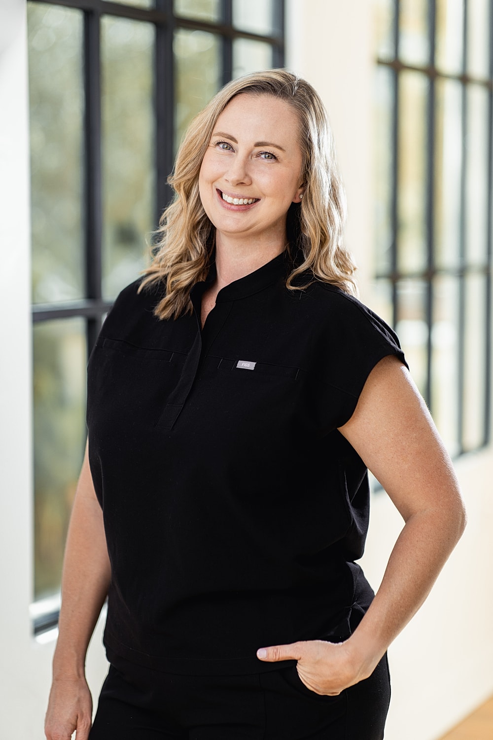Smiling woman in black outfit by window.
