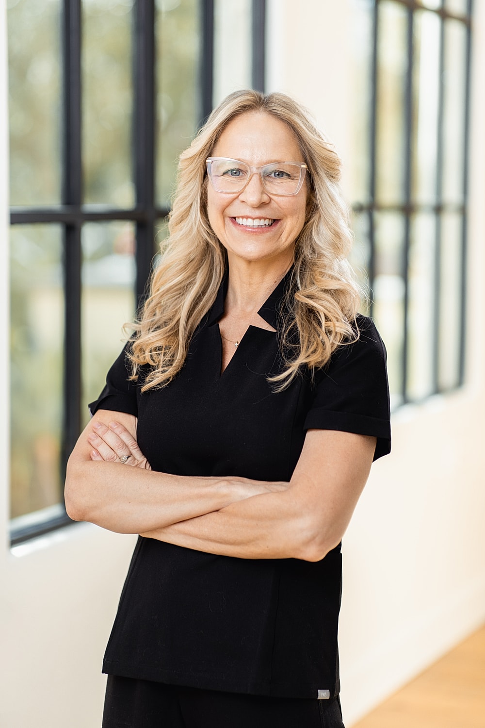 Smiling woman in black outfit with arms crossed.