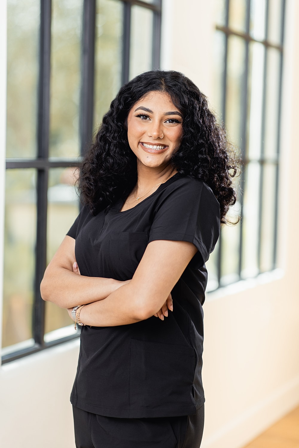 Smiling woman in black scrubs with crossed arms.