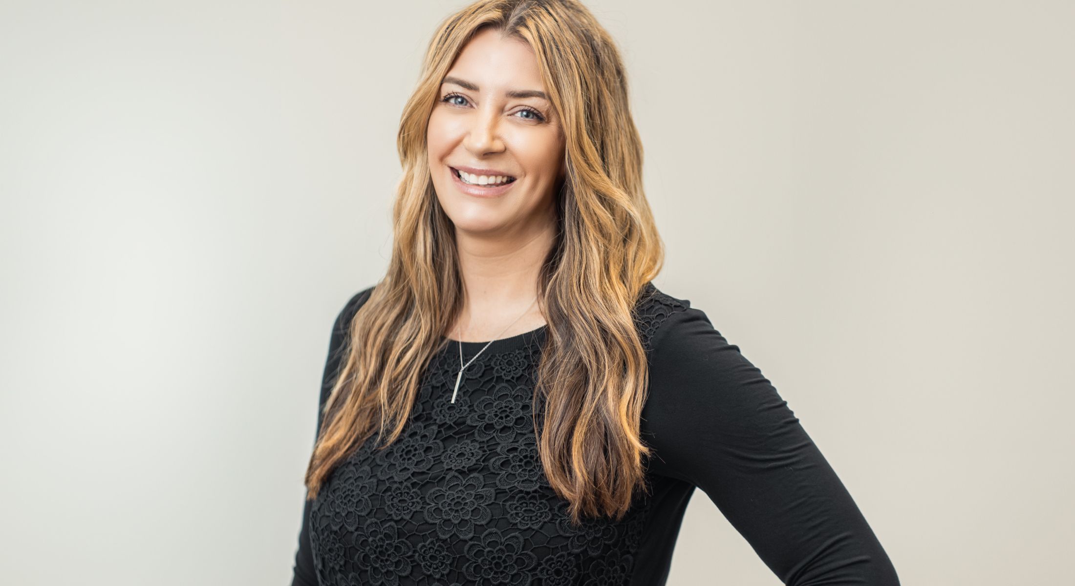 Smiling woman in black top against neutral background.