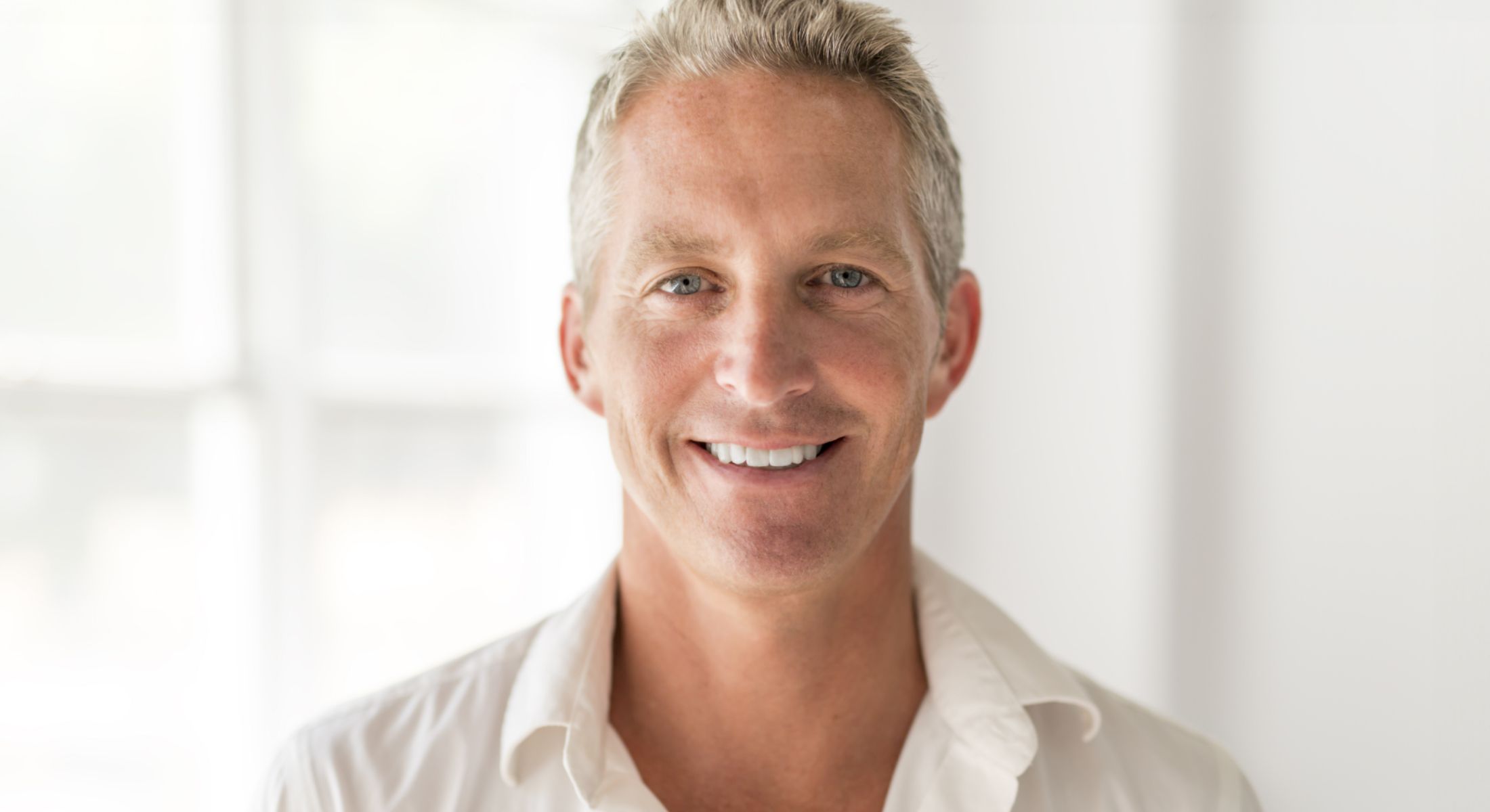 Smiling man in a white shirt, indoor setting.